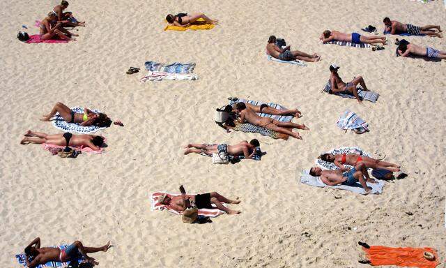 Beachgoers lie on their towels on Tamarama beach during a hot spring day in Sydney