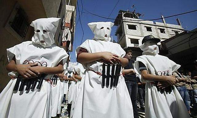 Masked Palestinian children, wearing  mock explosive belts and holding Korans, flash victory signs as