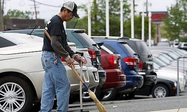 An employee at a Washington-area Chrysler dealership sweeps the ground at an outdoor car lot in New C