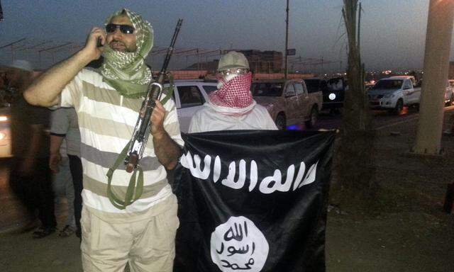 A fighter of the ISIL holds a weapon while another holds a flag in Mosul