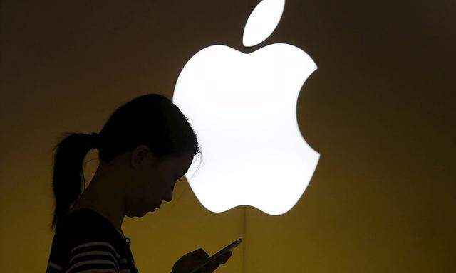 File photo of a woman looking at the screen of her mobile phone in front of an Apple logo outside an Apple store in downtown Shanghai