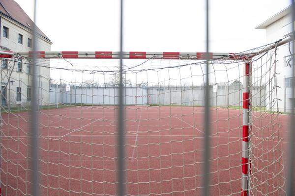 Fußball im Käfig, hinter der Mauer mit Stacheldraht, beobachtet von Beamten.