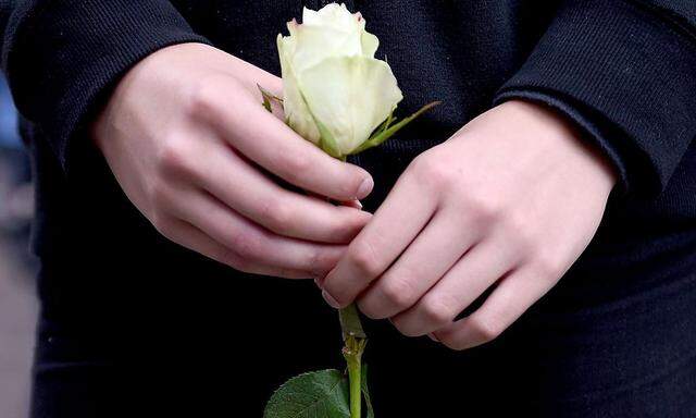 Ein junges Mädchen hält eine Rose in Gedenken an die Opfer.
