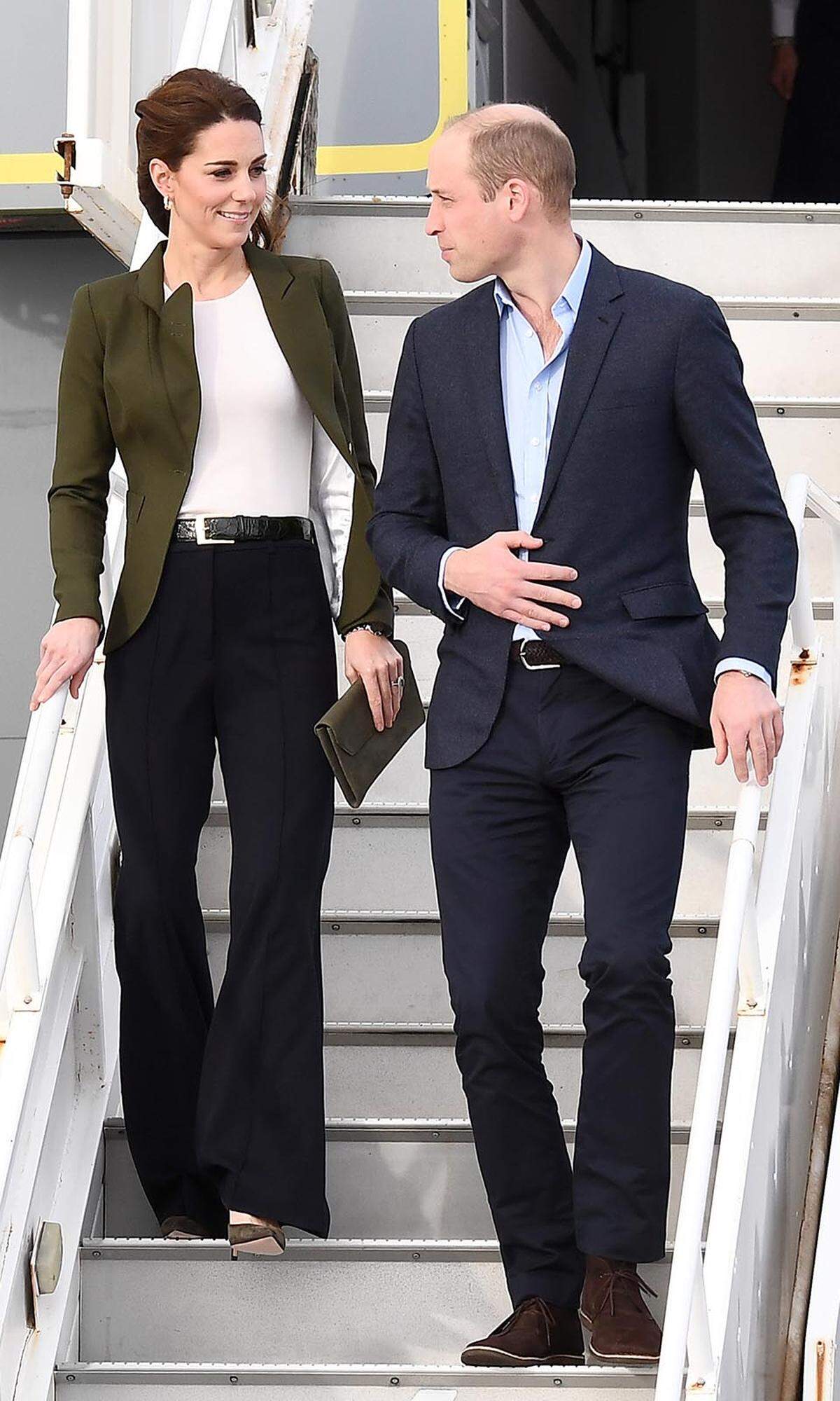 Kleine Fashion-Sensation im Hause Cambridge: Dass Kate ab und zu die Hosen an hat, ist jetzt nicht unbedingt neu, aber diese Kombi aus elegantem Blazer („Duchess Wool Blazer“ in Olivgrün von Smythe) und weiter Anzughose („High-Waisted Sport Luxe Trousers“ in Navy Blau von Jigsaw), mit der Kate gut begürtelt auf Zypern aus dem Flugzeug stieg, überraschte dann doch. Ob wohl jemand Anleihe im Kleiderschrank von Schwägerin Meghan genommen hat? Olivgrün war jedenfalls auch die Farbwahl für die Pumps (von Gianvito Rossi) und die Tasche („Dora“ Clutch von L.K. Benett). Ein Half-Bun gibt den Blick auf die „Oak Leaf Earrings“ von Asprey frei. Gut gelaunt waren die Cambridges allemal. Bei einem gemeinsamen Foto vor einem festlich dekorierten Christbaum scherzte William, seine Frau tarne sich geschickt – eine Anspielung auf Kates Blazer. Was haben wir gelacht...