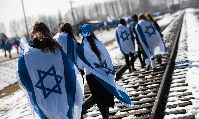 People wear Israeli flags around their shoulders as they  walk on the railroad tracks inside the former Nazi death camp of Birkenau