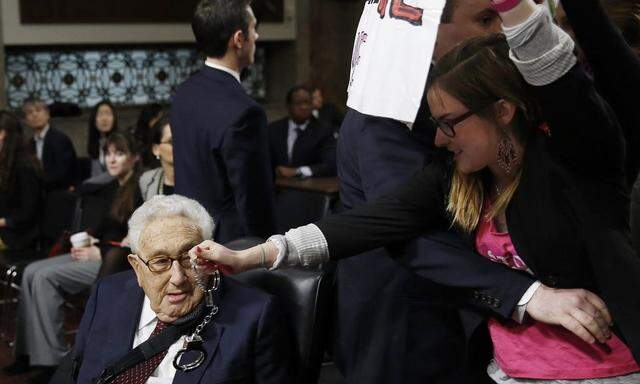 A Code Pink demonstrator dangles a set of handcuffs in front of former Secretary of State Kissinger at the Armed Services Committee on global challenges and U.S. national security strategy on Capitol Hill in Washington