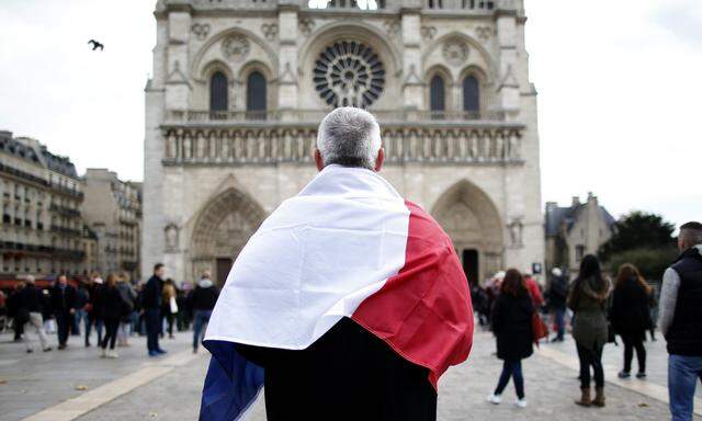 A man, wrapped with a French flag, observes a minute of silence at the Notre Dame Cathedral in Paris to pay tribute to victims of Friday´s Paris attacks