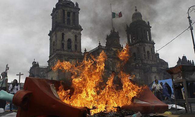 Members of the teachers' union CNTE and protesters stand near a burning barricade before they are evicted from Zocalo Square by the riot police in downtown Mexico City