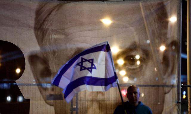 Ein Mann hält eine israelische Flagge, während er vor einem großen Bild des israelischen Premierministers Benjamin Netanjahu steht.