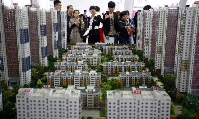 A sales assistant talks to visitors in front of models of apartments at a real estate exhibition in Shenyang