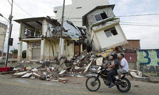 Men ride a motorcycle past damaged buildings in Pedernales