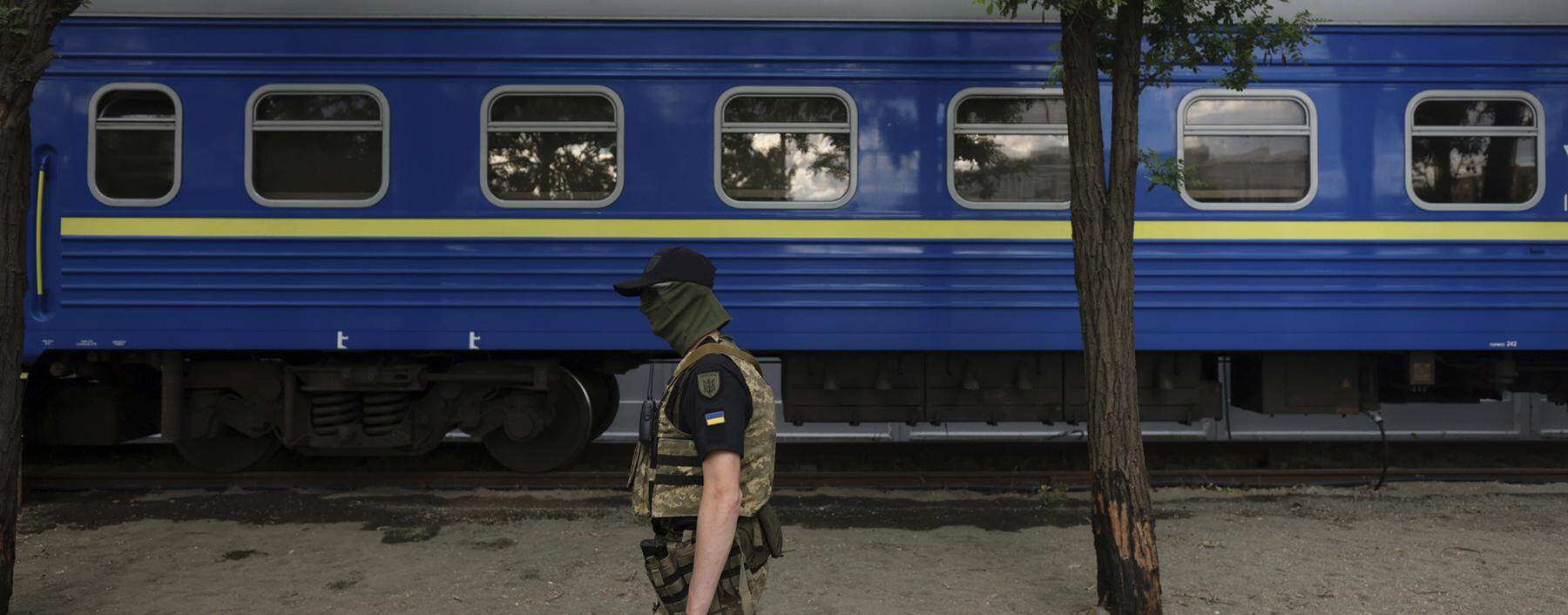 Ejn Soldat vor einem der blauen Waggons der ukrainischen Eisenbahn: Der Staatskonzern gilt  wegen seiner logistischen Schlüsselrolle als „zweite Armee“. 