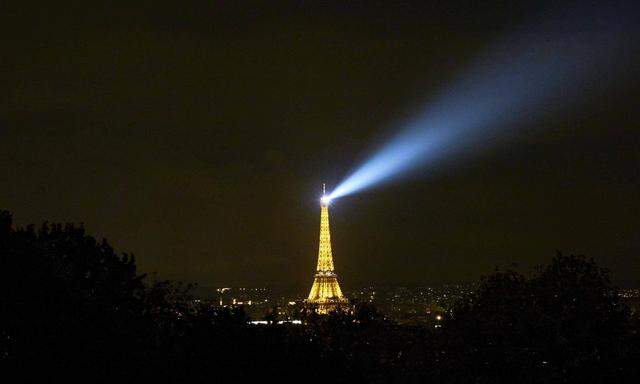 Der Eiffelturm leuchtet nachts mit seinen Lichtstrahlen über Paris.