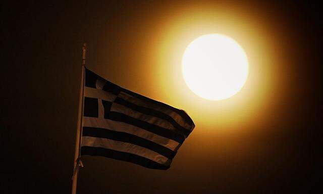 A Greek flag flutters atop the Greek Parliament as a full moon rises in central Athens