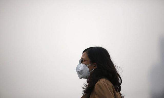 A woman wearing a mask walks on a street on a hazy day in Beijing