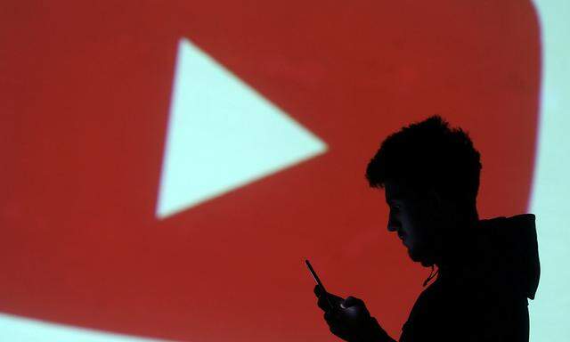 Silhouette of mobile user is seen next to a screen projection of Youtube logo in this picture illustration