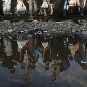 Syrian refugees are reflected in a puddle as they wait at the Greek-Macedonian border