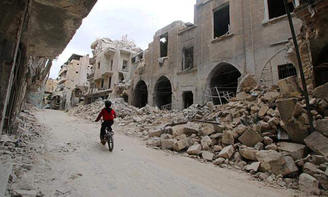 A boy rides a bicycle near damaged buildings in the rebel held area of Old Aleppo
