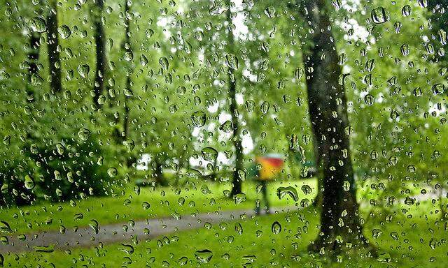 Raindrops are pictured on a car windscreen as person walks in a park on a rainy day in Bregenz