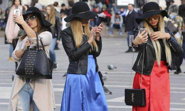 Women use their mobile phones in Duomo Square in downtown Milan