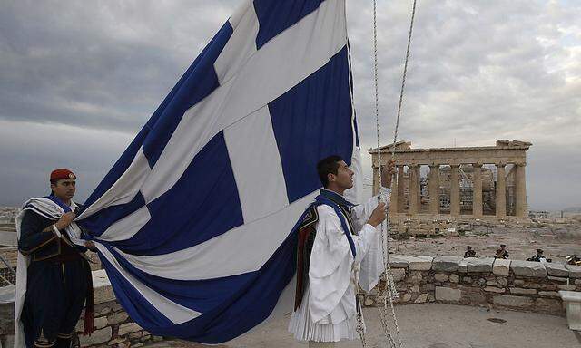 Greek Presidential Guards hoist the Greek flag in front of the Parthenon temple at the Acropolis hill in Athens