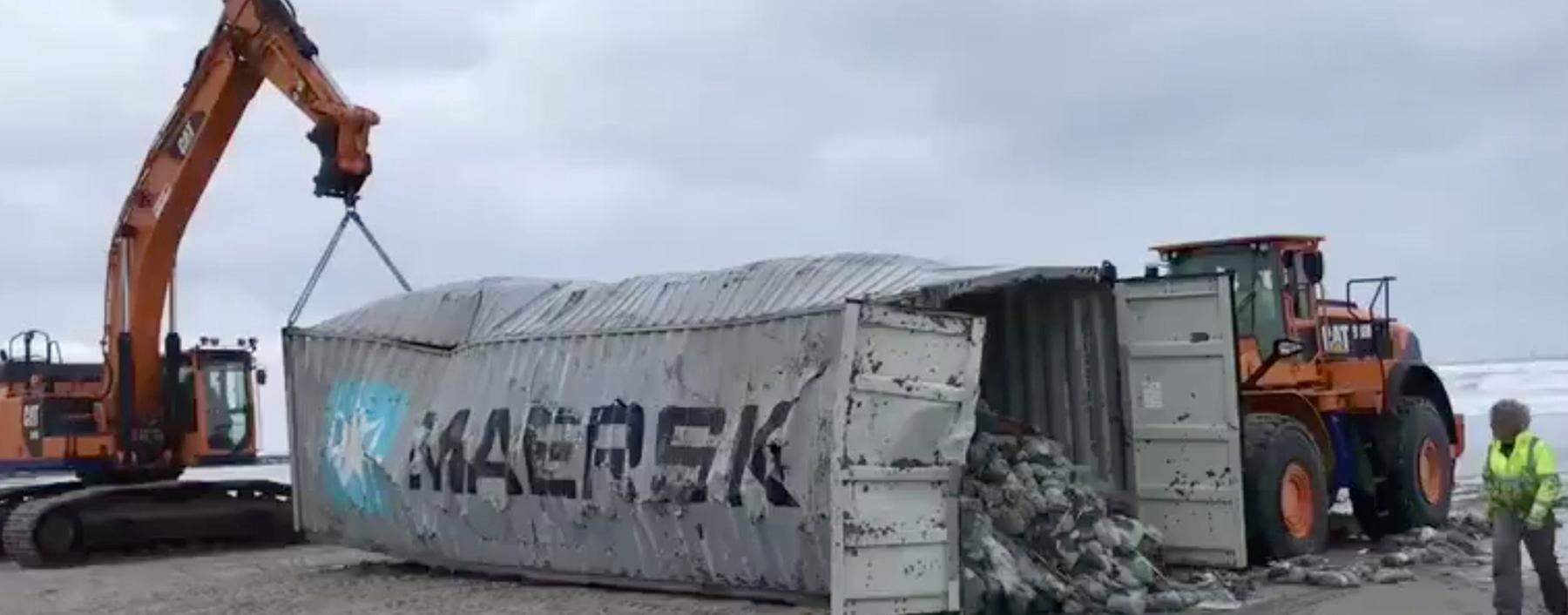 Heavy machinery lift cargo container after it washed up on beach in Vlieland