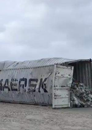 Heavy machinery lift cargo container after it washed up on beach in Vlieland