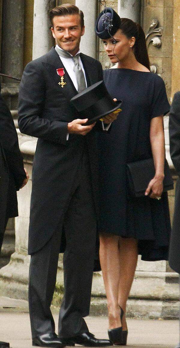 In ein elegantes, dunkles Kleid gehüllt und Hut auf dem Kopf bzw. mit einem Orden der Königin geschmückt und einem Zylinder in der Hand sind Victoria und David Beckham vor der Westminster Abbey eingetroffen.