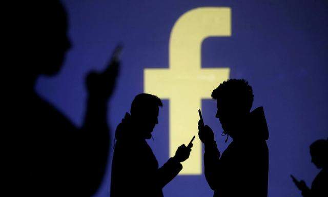 FILE PHOTO: Silhouettes of mobile users are seen next to a screen projection of Facebook logo in this picture illustration