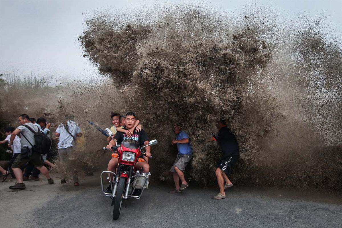 Schaulustige flüchten vor einer hohen Welle am Qiantang Fluss in Hangzhou, China.