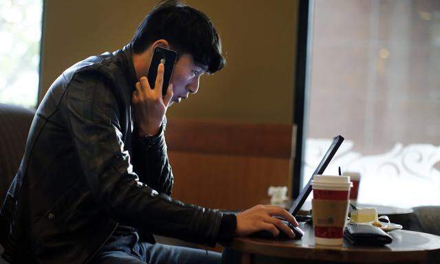 A man talks on the phone as he surfs the internet on his laptop at a local coffee shop in downtown Shanghai