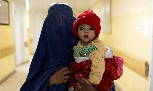 A mother wearing a burqa walks with a baby at the malnutrition ward at the Indra Gandhi hospital in Kabul