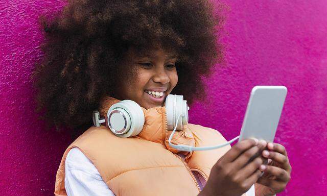 Girl wearing headphones using mobile phone leaning on pink wall model released, Symbolfoto, PNAF04086