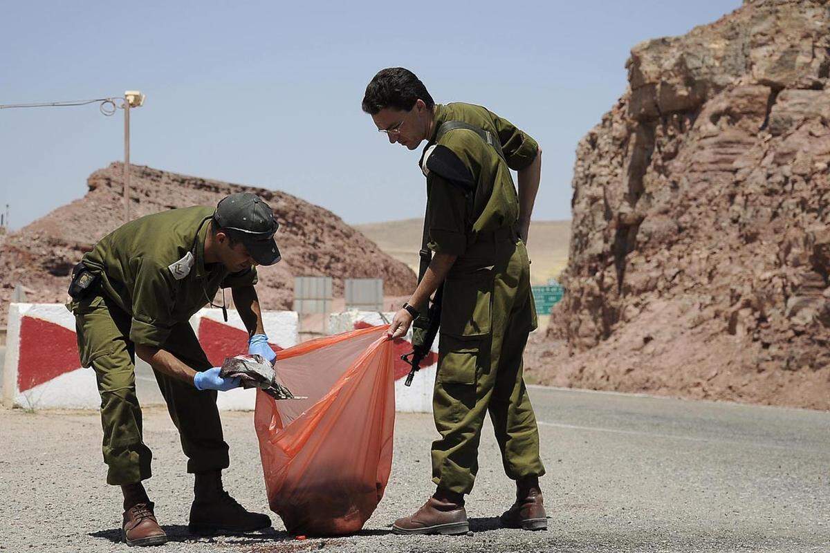 Soldaten sammeln auf der Straße blutverschmierte Kleidungsstücke ein.
