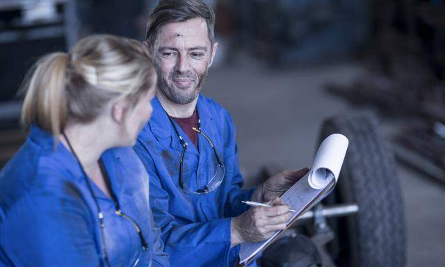Man and woman wearing blue overalls in workshop man with clipboard model released Symbolfoto proper