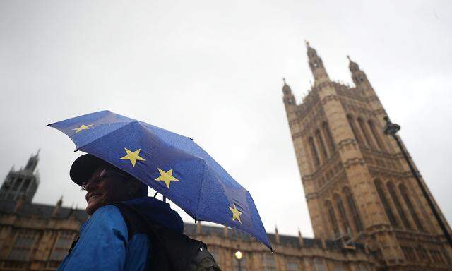 An anti-Brexit protester shelters under an EU flag themed umbrella opposite the Houses of Parliament in London