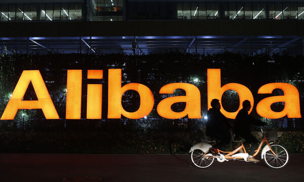 File photo of people riding a double bicycle past a logo of The Alibaba Group at the company´s headquarters on the outskirts of Hangzhou