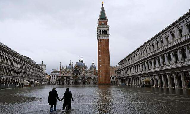 A couple walks in flooded St. Mark´s Square during high tide as the flood barriers known as Mose are not raised, in Venice