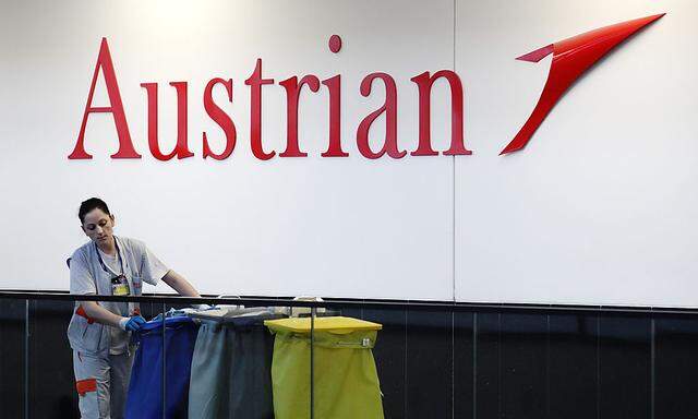 A cleaning woman passes an Austrian Airlines logo at the airport in Schwechat