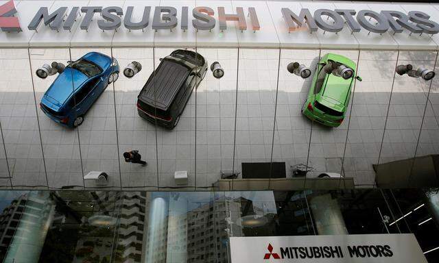 Mitsubishi Motors Corp´s vehicles and a passer-by reflected on an external wall at the company headquarters in Tokyo