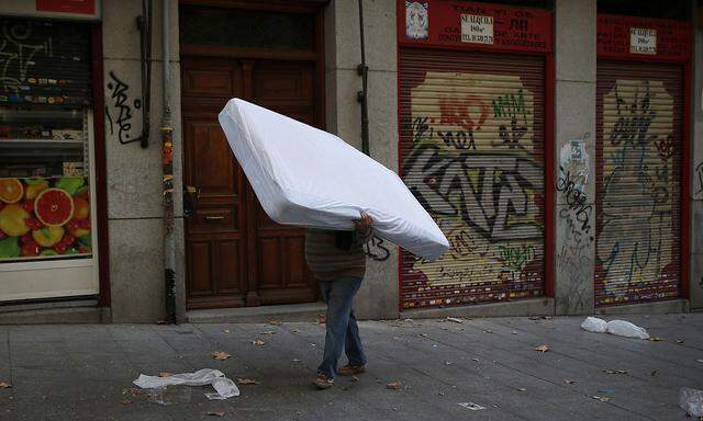A man carries a mattress on his head as he walks to throw garbage during the ongoing street cleaning unions´ strike in Madrid
