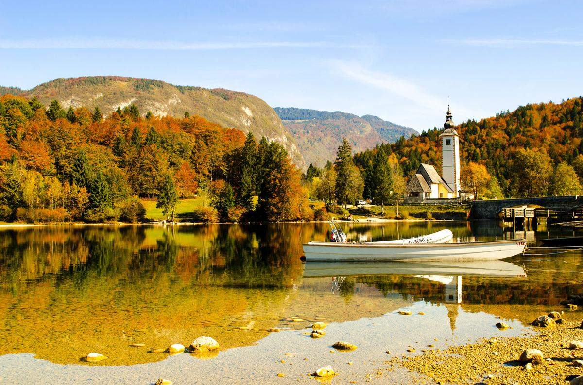 Umgeben von majestätischen Berghängen und der Kirche sv. Janez befindet sich der See Bohinjsko Jezero im Triglav-Nationalpark. Die prächtigen Wälder spiegeln sich im See und sorgen für ein besonders schönes Bild.