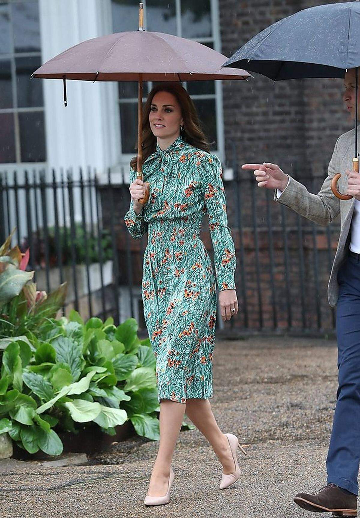 Für den Gartenbesuch kleidete sich Kate wie üblich dem Thema entsprechend: grün und frisch und mit Pflanzenmotiven - und ein bisschen zu sommerlich für den Augustregen. Das gemusterte Prada-Kleid dürfte wohl unter der Annahme gekauft worden sein, dass das Londoner Wetter ein! Mal! mitspielen werde. Das hochgeschlossene Teil steht der Herzogin dennoch ausgezeichnet. (Findet eigentlich noch jemand, das Kate mit dem Look aussieht wie ihre Schwester Pippa?)