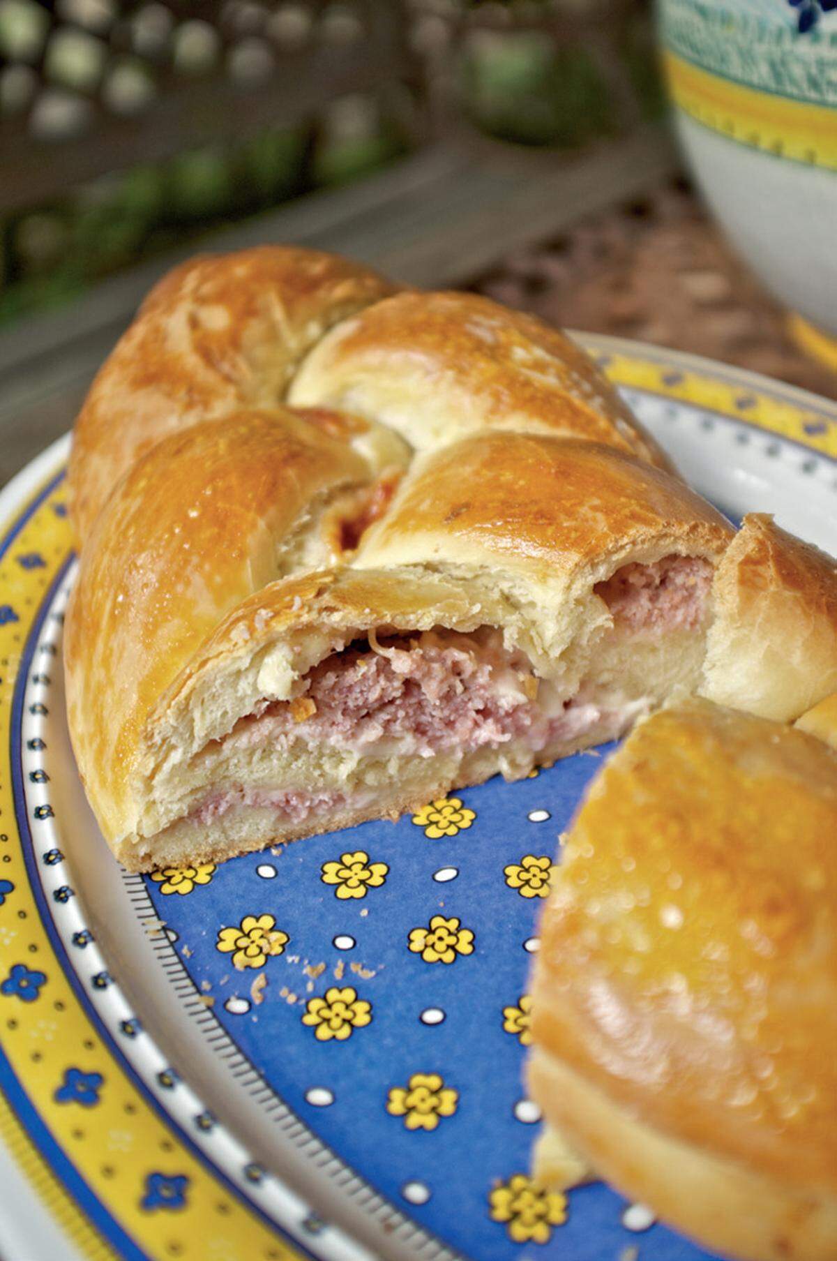 Den Teig in drei gleiche Teile teilen und daraus flache Streifen formen. Schinken und Käse in kleinen Stücken auf die drei Streifen legen und sie einrollen, sodass man drei Teigrollen erhält. Die Teigrollen nebeneinander auf Backpapier legen und ihre oberen Enden zusammendrücken. Dann aus den Rollen einen Zopf flechten, indem man sie abwechselnd übereinanderlegt. Die drei unteren Enden ebenfalls zusammendrücken und das Backpapier mit dem Zopf auf ein Blech legen. Etwa zwei Stunden an einem lauwarmen Ort gehen lassen. Anschließend den Zopf mit einem Eigelb bestreichen und bei 180–200 °C für 40 Minuten im Ofen backen. Etwas abkühlen lassen und lauwarm servieren.