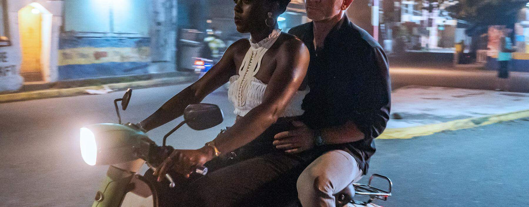 Kein alltäglicher Anblick: James Bond (Daniel Craig) als Beifahrer auf einem Moped im neuen Film „Keine Zeit zu sterben“. Am Steuer: Lashana Lynch.