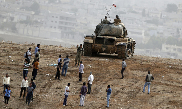 A Turkish officer warns Kurds watching over the Syrian town of Kobani to leave the top of a hill near Mursitpinar border crossing in the southeastern Turkish town of Suruc