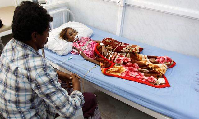 Father of malnourished girl Jamila Ali Abdu sits as she lies on a hospital bed before she died in the Red Sea port city of Hodeidah