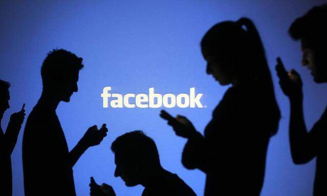 File illustration photo of people silhouetted as they pose with mobile devices in front of a screen projected with a Facebook logo