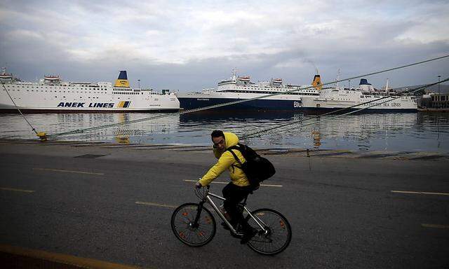 A man rides his bicycle as passengers ships are moored during a 24-hour general strike against planned pension reforms at the port of Piraeus
