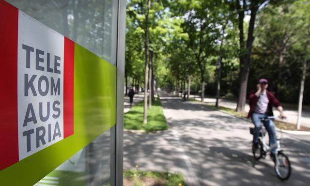 A cyclist talks on his mobile phone as he passes a Telekom Austria phone booth in Vienna